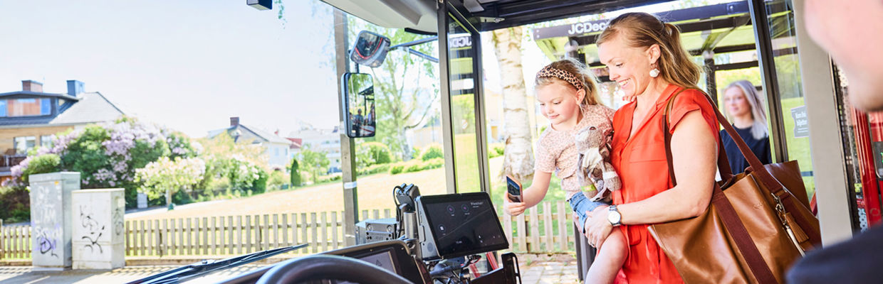En bild som visar en mamma och hennes dotter. De går på bussen och dottern blippar en biljett.