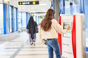 En ung kvinna står framför en biljettautomat inne på Nässjö station. Kvinnan använder biljettautomaten och gör olika val på skärmen.