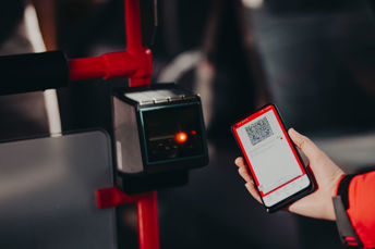 Närbild på resenär som håller sin mobil i handen och blippar sin bussbiljett ombord på en buss.